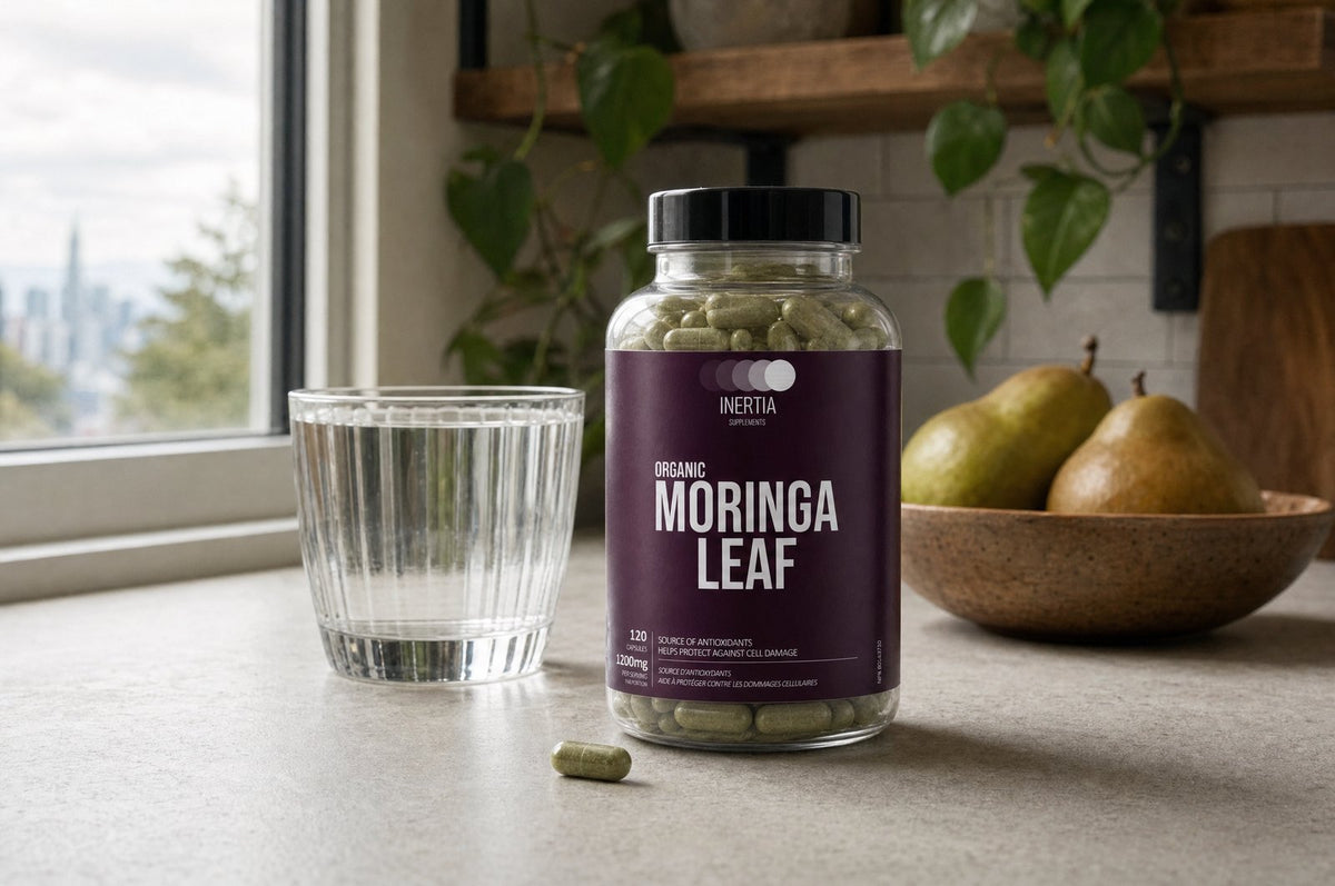 A bottle of Inertia Supplements Moringa Leaf on a kitchen counter in morning light, beside a glass of water and one capsule